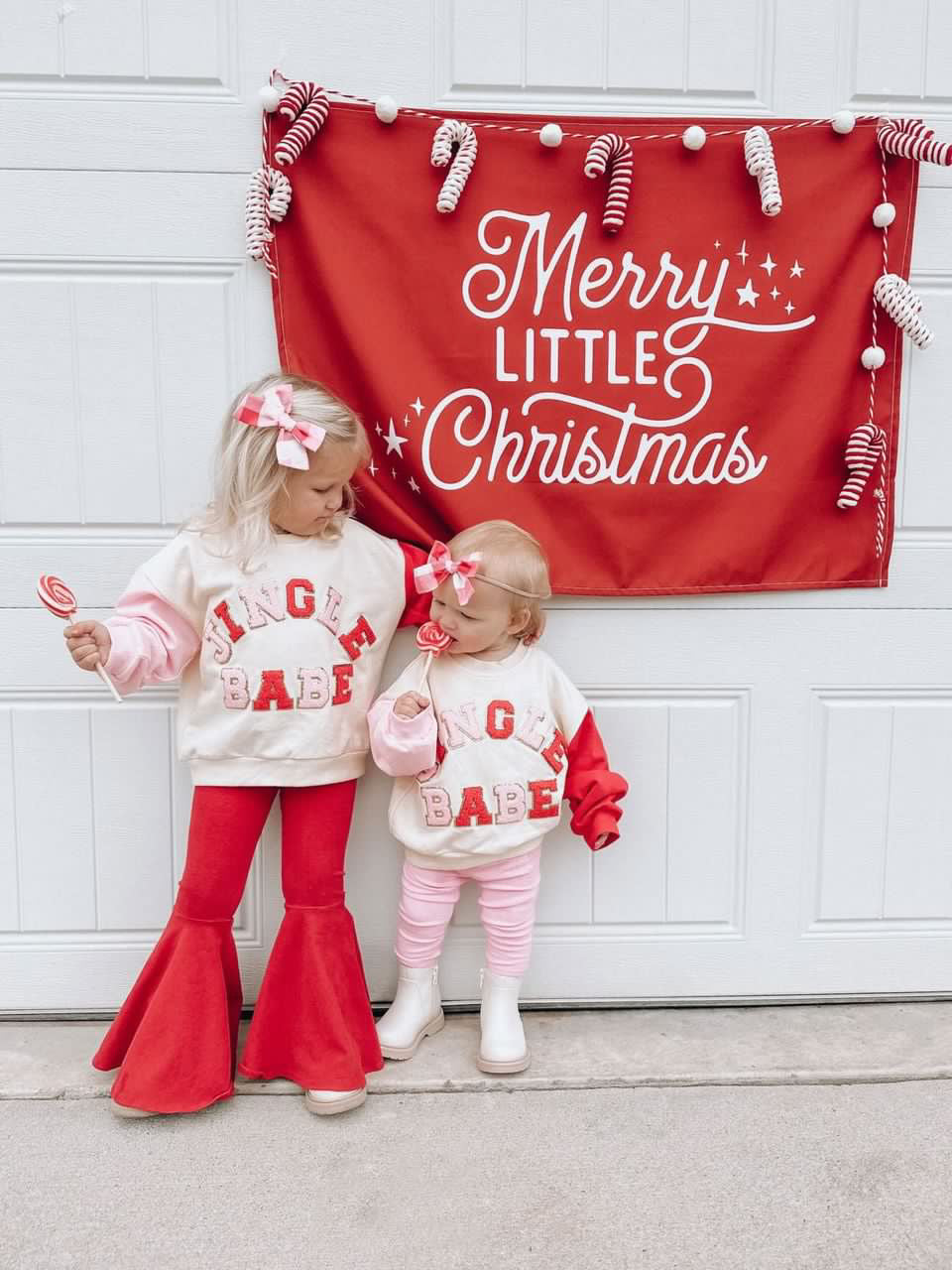 Two children in matching christmas outfits with a 'Merry Little Christmas' banner in the background